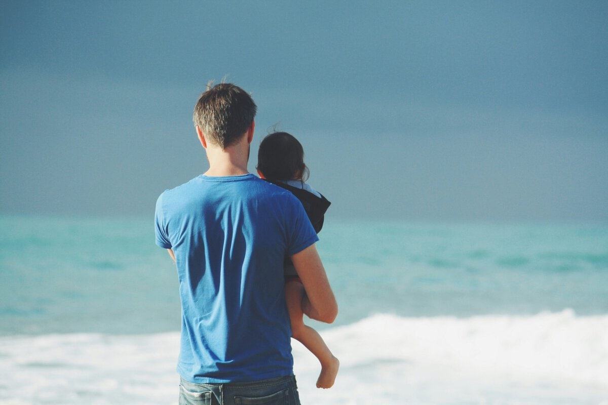 Father holding daughter at the beach with ocean waves in background.